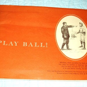 May include: An orange vintage baseball rules booklet with the text "PLAY BALL!" in gold lettering. An oval illustration depicts two men in baseball attire. Additional text includes rules and regulations.
