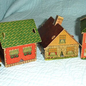 Puede incluir: Una colecci&oacute;n de casas de papel vintage en varios estilos. Las casas presentan dise&ntilde;os de ladrillo rojo, tejas verdes y tejados marrones. Cada casa tiene ventanas y chimeneas detalladas, creando un encantador pueblo en miniatura.