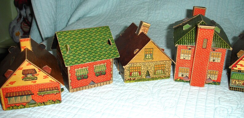 Puede incluir: Una colecci&oacute;n de casas de papel vintage en varios estilos. Las casas presentan dise&ntilde;os de ladrillo rojo, tejas verdes y tejados marrones. Cada casa tiene ventanas y chimeneas detalladas, creando un encantador pueblo en miniatura.