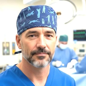 May include: A blue scrub cap featuring a repeating pattern of light blue silhouettes of people playing golf in various stances. The cap is made of fabric and has a fitted design that covers the top of the head, worn with a matching blue scrub top.