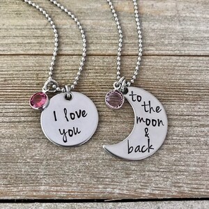 Puede incluir: Dos collares de plata con dijes. Un dije dice "Te amo" y el otro dije es una luna creciente que dice "hasta la luna y de regreso".