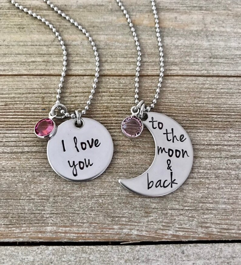 Puede incluir: Dos collares de plata con dijes. Un dije dice "Te amo" y el otro dije es una luna creciente que dice "hasta la luna y de regreso".