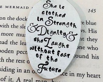 May include: Silver tone metal charm with an inspirational quote: "She is clothed in Strength & Dignity & she laughs without fear of the future".