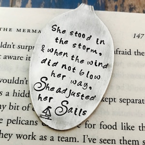 May include: A silver spoon with an inspirational quote engraved on it. The quote reads "She stood in the storm, & when the wind did not blow her way, She adjusted her sails."