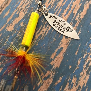May include: A yellow and red fishing lure with a silver charm that reads "You are my greatest catch".
