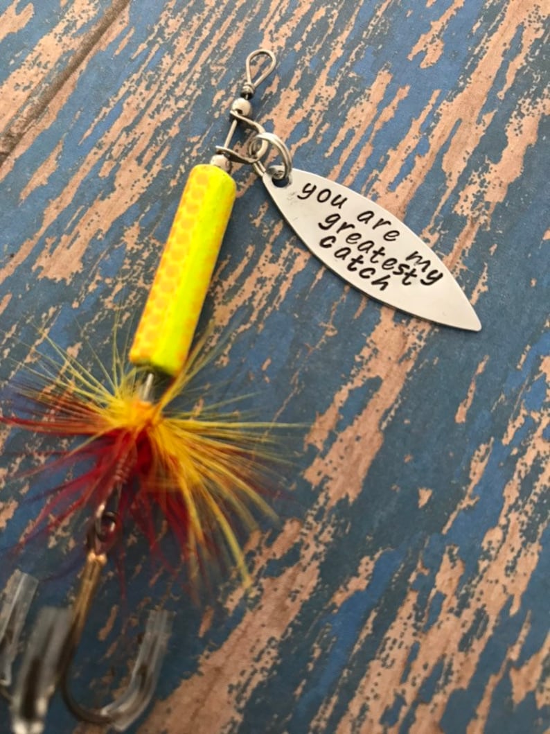 May include: A yellow and red fishing lure with a silver charm that reads "You are my greatest catch".