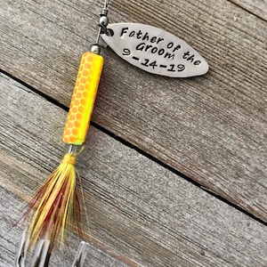 Pu&ograve; includere: Un'esca da pesca argentata con un corpo giallo e arancione e piume rosse e gialle. L'esca ha un'etichetta argentata che dice "Father of the Groom 9-14-19".