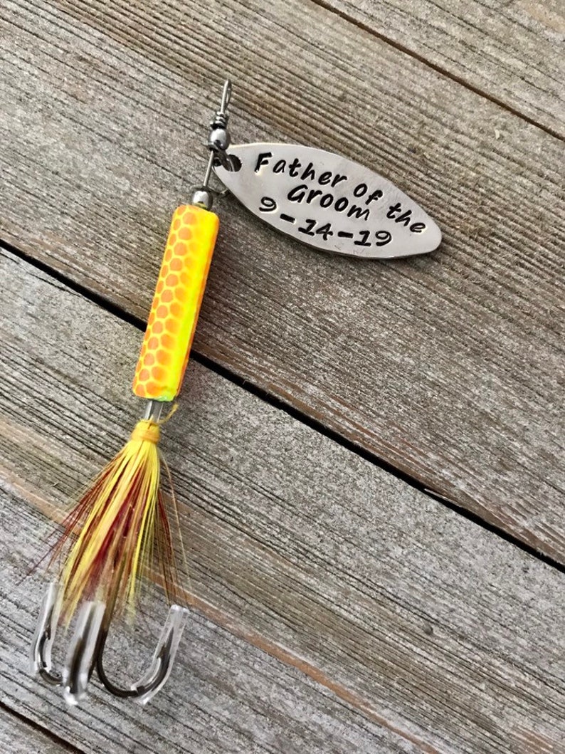 Pu&ograve; includere: Un'esca da pesca argentata con un corpo giallo e arancione e piume rosse e gialle. L'esca ha un'etichetta argentata che dice "Father of the Groom 9-14-19".