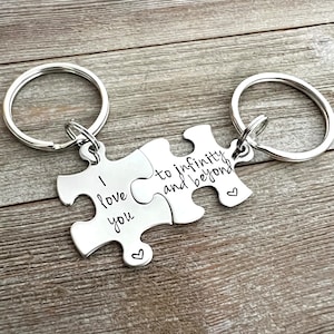 May include: Two silver puzzle piece keychains with a heart design. One piece says "I love you" and the other says "to infinity and beyond".