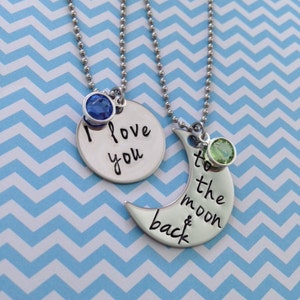 Puede incluir: Dos collares de plata con dijes. Un dije es un c&iacute;rculo con el texto "Te amo" y una piedra preciosa azul. El otro dije es una luna creciente con el texto "hasta la luna y de regreso" y una piedra preciosa verde.