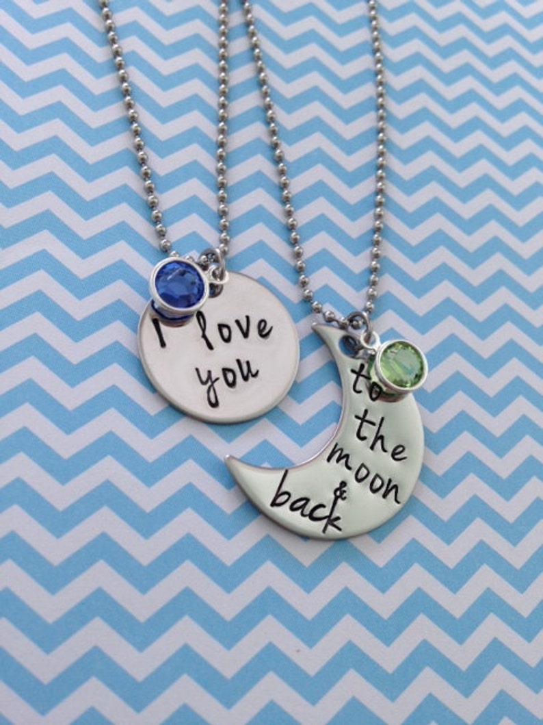 Puede incluir: Dos collares de plata con dijes. Un dije es un c&iacute;rculo con el texto "Te amo" y una piedra preciosa azul. El otro dije es una luna creciente con el texto "hasta la luna y de regreso" y una piedra preciosa verde.