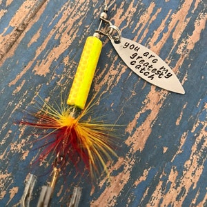 May include: A yellow and red fishing lure with a silver charm that reads "You are my greatest catch".