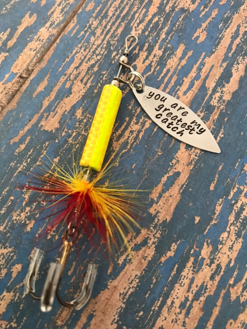 May include: A yellow and red fishing lure with a silver charm that reads "You are my greatest catch".