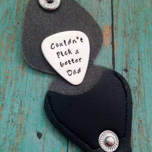 May include: A silver guitar pick keychain with a black leather case. The pick has the text "Couldn't pick a better Dad" engraved on it.