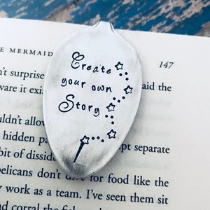 May include: A silver spoon bookmark with the text "Create your own Story" engraved on it. The spoon has a star design and a small wand.