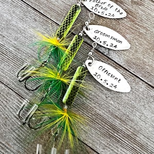 Pu&ograve; includere: Tre esche da pesca con piume verdi e gialle e ami argentati. Ogni esca ha un'etichetta argentata con il testo "Father of the Bride 10.5.24", "Groomsman 10.5.24" e "Officiant 10.5.24".