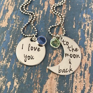 Puede incluir: Dos collares de plata con dijes. Un dije es un c&iacute;rculo con el texto "Te amo" y una piedra preciosa azul. El otro dije es una luna creciente con el texto "hasta la luna y de regreso" y una piedra preciosa verde.