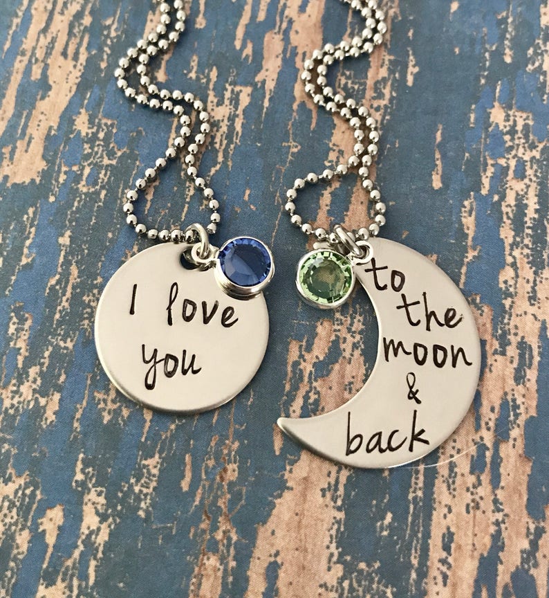 Puede incluir: Dos collares de plata con dijes. Un dije es un c&iacute;rculo con el texto "Te amo" y una piedra preciosa azul. El otro dije es una luna creciente con el texto "hasta la luna y de regreso" y una piedra preciosa verde.