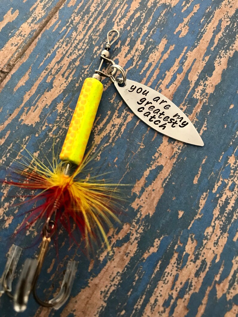May include: A yellow and red fishing lure with a silver charm that says "You are my greatest catch".