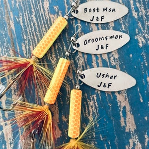 Pu&ograve; includere: Tre esche da pesca con etichette personalizzate che recitano "Best Man J&F", "Groomsman J&F" e "Usher J&F". Le esche sono arancioni e gialle con piume.