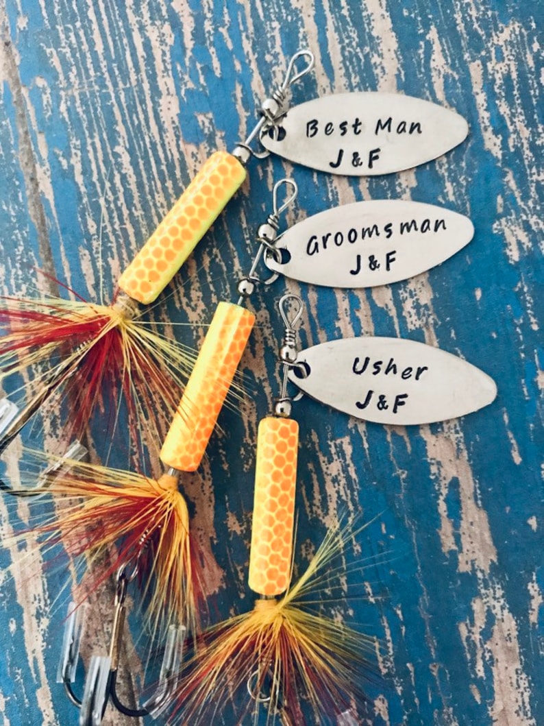 Pu&ograve; includere: Tre esche da pesca con etichette personalizzate che recitano "Best Man J&F", "Groomsman J&F" e "Usher J&F". Le esche sono arancioni e gialle con piume.