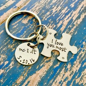 May include: Gold-toned keychain with two charms. One charm is a round disc with the text "mc & dt 5.20.16". The other charm is a puzzle piece with the text "I love you most".