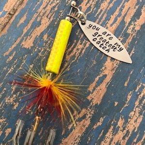 May include: A yellow and red fishing lure with a silver charm that reads "You are my greatest catch".
