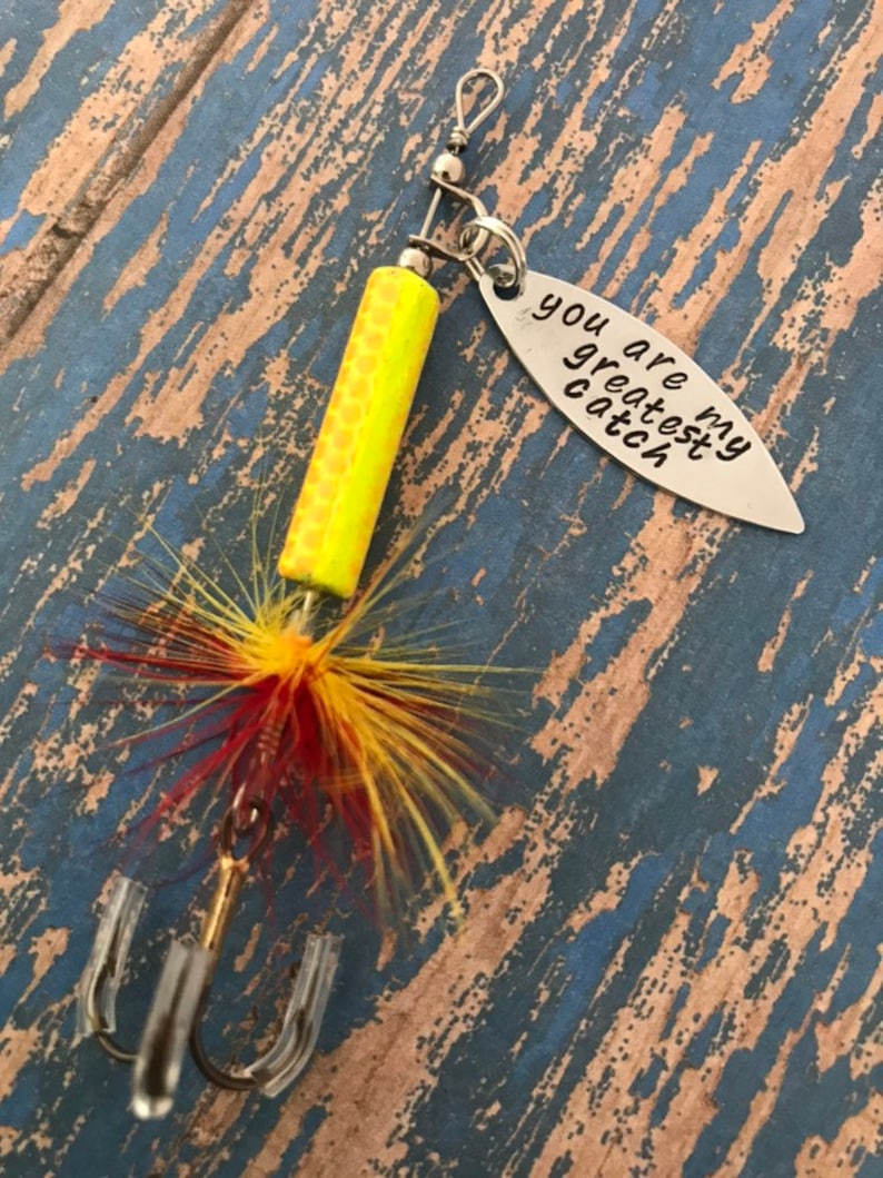 May include: A yellow and red fishing lure with a silver charm that reads "You are my greatest catch".