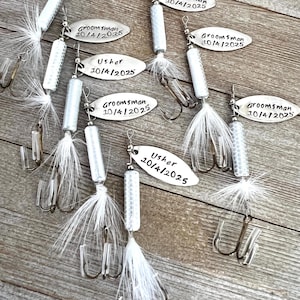 Pu&ograve; includere: Un set di otto esche da pesca argentate con piume bianche. Ogni esca ha un'etichetta ovale argentata con il testo "Groomsman" o "Usher" e una data.