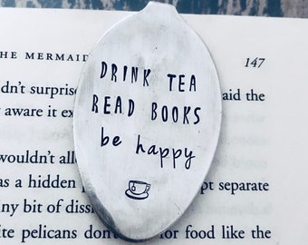 May include: Silver bookmark with the text "Drink Tea Read Books Be Happy" and a small teacup icon.