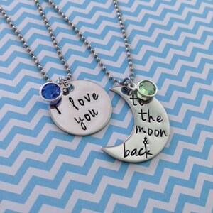 Puede incluir: Dos collares de plata con dijes. Un dije es un c&iacute;rculo con el texto "Te amo" y un cristal azul. El otro dije es una luna creciente con el texto "hasta la luna y de regreso" y un cristal verde.