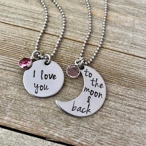 Puede incluir: Dos collares de plata con dijes a juego. Un dije es un c&iacute;rculo con el texto "Te amo" y el otro es una luna creciente con el texto "hasta la luna y de regreso".
