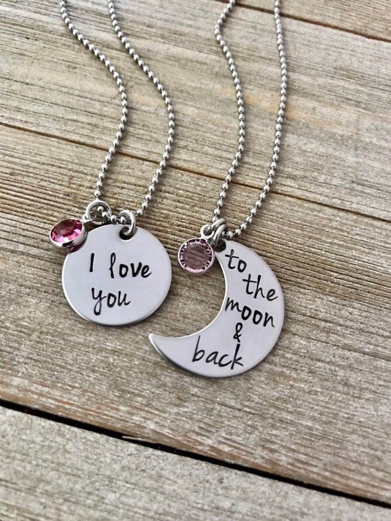 Puede incluir: Dos collares de plata con dijes a juego. Un dije es un c&iacute;rculo con el texto "Te amo" y el otro es una luna creciente con el texto "hasta la luna y de regreso".