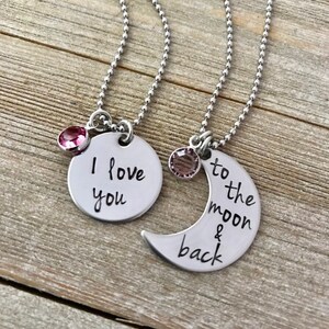 Puede incluir: Dos collares de plata con colgantes a juego. Un colgante es un c&iacute;rculo con las palabras "Te amo" y el otro es una luna creciente con las palabras "hasta la luna y de regreso".