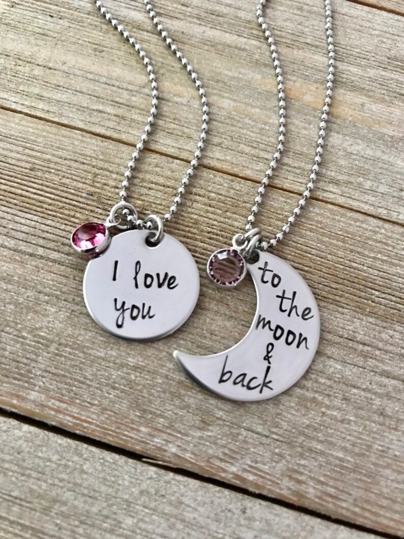 Puede incluir: Dos collares de plata con colgantes a juego. Un colgante es un c&iacute;rculo con las palabras "Te amo" y el otro es una luna creciente con las palabras "hasta la luna y de regreso".