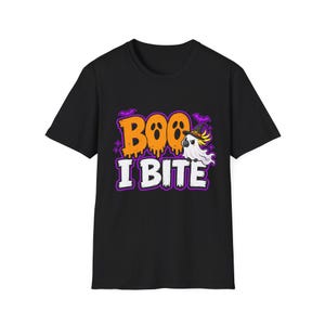 Pode incluir: Uma t-shirt preta de manga curta com uma estampa gráfica contendo o texto laranja BOO e o texto branco I BITE. O design inclui uma cacatua branca usando um chapéu de bruxa preto, morcegos roxos e pequenos detalhes de estrelas roxas.