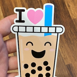 May include: A sticker with the text "I love" and a pink heart next to it. The sticker also features a cartoon illustration of a brown bubble tea cup with a blue straw, a smiling face, and black boba pearls.