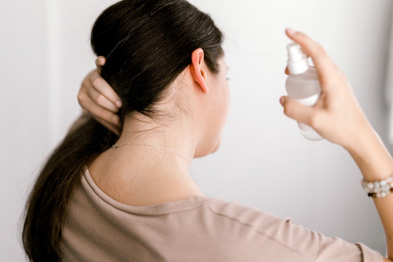 May include: A person with long brown hair is spraying a clear bottle of hair product on their hair.