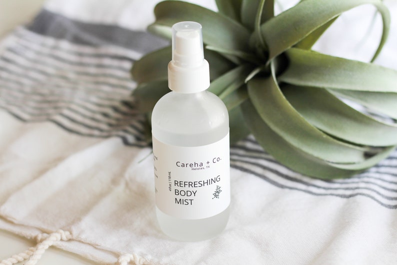 May include: A clear glass bottle with a white spray top and a white label that reads "Careha + Co. Houston, TX Refreshing Body Mist 4 fl oz / 118 ml".