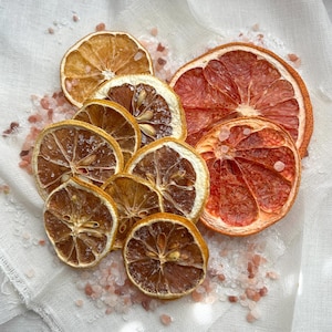 May include: Dried citrus fruit slices, including lemons and grapefruits, arranged on a white surface with pink Himalayan salt.