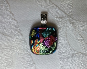 May include: A square-shaped glass pendant with a silver bail. The glass is black with iridescent green, blue, pink, and orange pieces.
