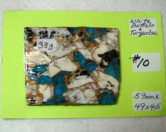 May include: A close-up of a piece of white buffalo turquoise with gold and black accents. The stone is 15 cm by 12.5 cm and 11.5 cm. The stone is labelled "#10" and "38g."