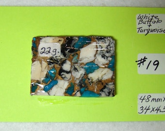 May include: A close-up of a white buffalo turquoise stone with a brown, black, and white pattern. The stone is 48 mm x 37 x 45 mm and weighs 22 grams. The stone is labelled "White Buffalo + Turquoise" and "#19".