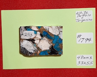 May include: A piece of white buffalo turquoise with blue and black veins. The stone is 48mm x 33 x 5.5mm and weighs 25g. It is labelled "White Buffalo + Turquoise" and "#1794".
