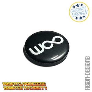 Könnte beinhalten: Ein schwarzer Knopf mit einem weißen "woo" Unendlichkeitssymbol. Der Knopf hat eine glänzende Oberfläche und befindet sich vor einem weißen Hintergrund. Der Text "ORIGINAL DESIGN" befindet sich in einem Kreis oben rechts.