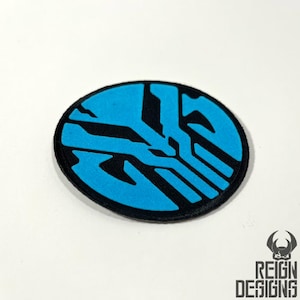 May include: A blue and black circular patch with a geometric design. The patch is made of fabric and has a stitched edge.