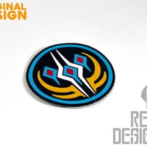 May include: A round, blue, yellow, white, and red embroidered patch with a stylized design of three white spikes with red squares at the base of each spike. The spikes are surrounded by a yellow crescent shape and a blue circle.