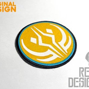 May include: A round, embroidered patch with a white symbol on a yellow background. The symbol is a stylized design with a sharp point at the top and curved lines on the sides. The patch has a blue border and a black backing.