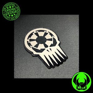 May include: A black and white embroidered patch featuring a stylized skull design integrated with a circular geometric emblem. The patch has a clean, sharp edge and a textured surface, displaying a high-contrast graphic motif that combines a skull shape with a central circular pattern.