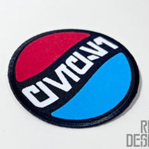 May include: A round patch with a black border, featuring a diagonal split of red and blue. The word "CIVIC" is printed in white, angled across the center. The patch is likely for clothing or accessories.